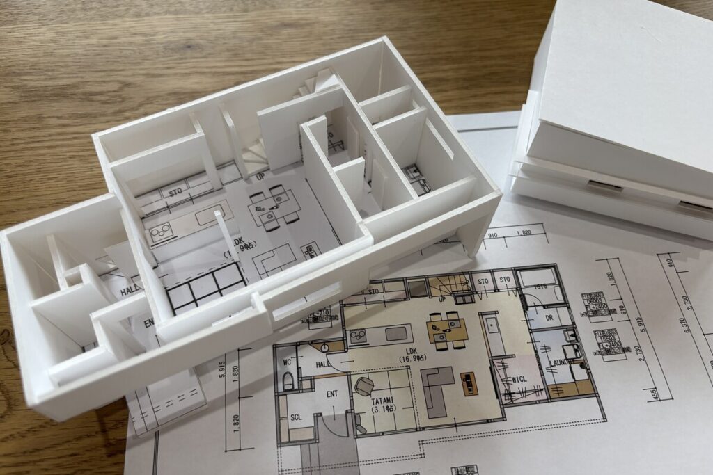 注文住宅の間取り図（平面図）の上に置かれた、白いスチレンボードで作られた平屋住宅の立体模型。図面だけでは分かりにくい空間の広がりや動線を視覚的に確認できます。