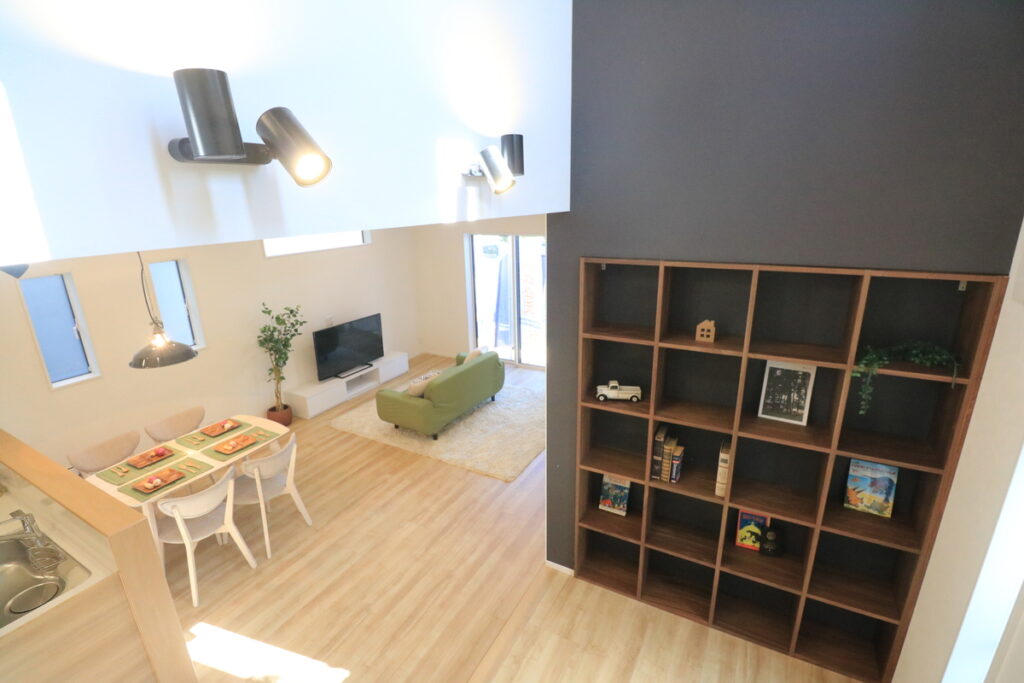 吹き抜けのあるリビングに設置された、天井までの高さを活かした大容量の木製壁面一体型収納棚。