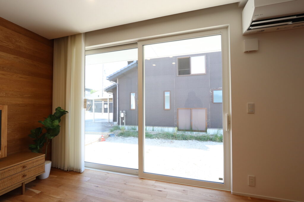 木目調のアクセントウォールがあるリビングに設置された、屋外の景色を大きく取り込む大開口の樹脂サッシの引き違い窓。