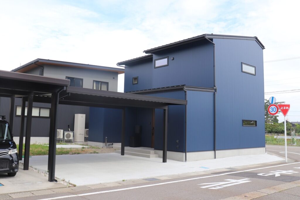 ネイビーのガルバリウム外壁が印象的なモダンな外観。2台分の駐車スペースを確保した黒いカーポートと、シャープな片流れ屋根のシルエットが落ち着いた佇まいを見せています。