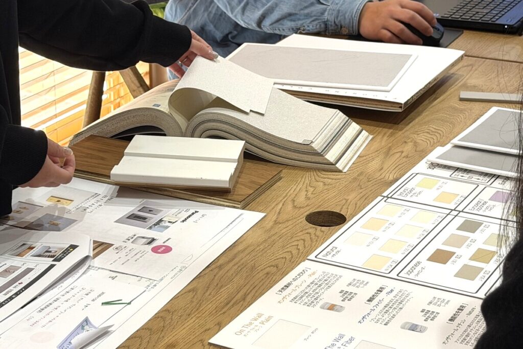 家づくりの打ち合わせにて、壁紙のサンプルブックやフローリングの端材、塗り壁のカラーチャートを広げて検討する様子。一つひとつの建材を手に取りながら、理想のインテリアイメージを具体化していく工程です。