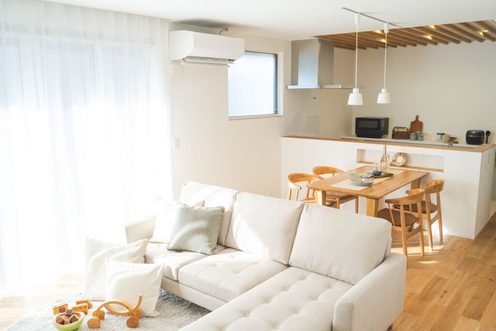 明るい光が差し込むナチュラルモダンなLDK。白い大判のソファが置かれたリビングから、木の温もりを感じるダイニングテーブルと対面式キッチンまでを見渡す開放的な空間です。