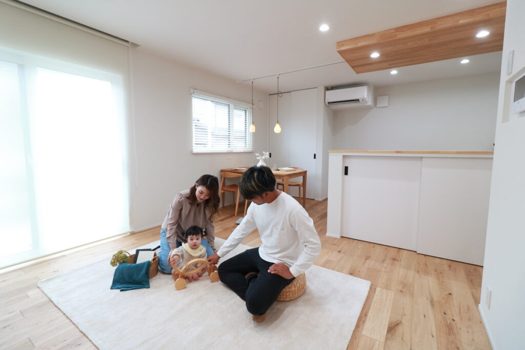 明るい光が差し込むリビングで、無垢の床に敷いたラグの上で仲睦まじく遊ぶ子育て世代の家族。