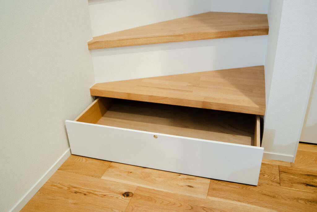 階段下スペースを有効活用した引き出し式の造作収納。白と木目を基調としたデザインで、デッドスペースになりがちな場所を実用的な収納場所に変える、注文住宅ならではの工夫です。