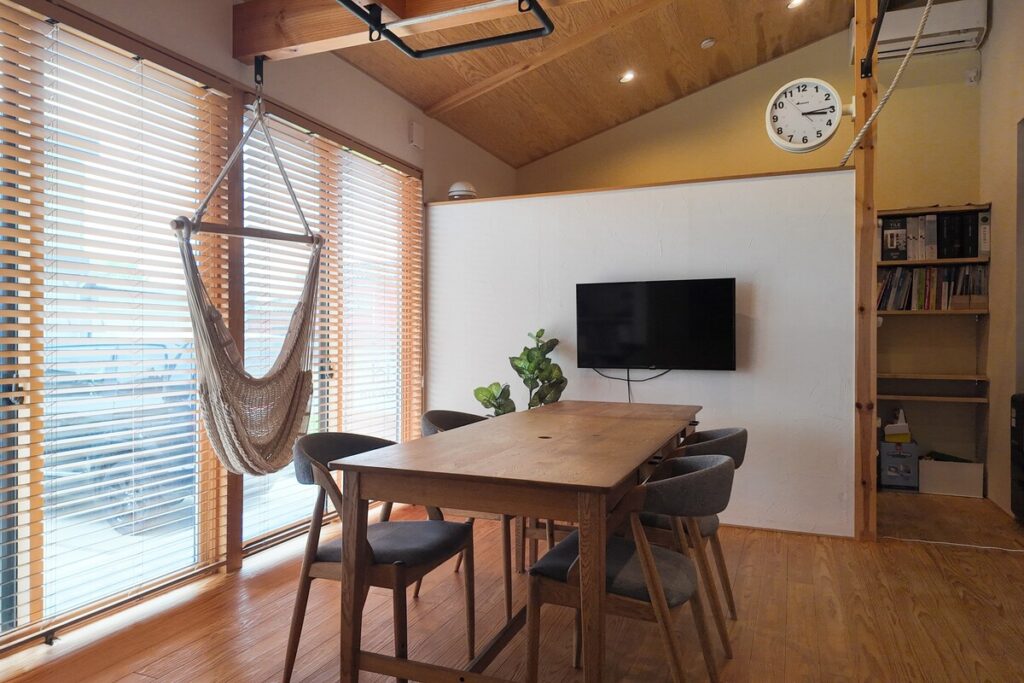 勾配天井の開放的な空間に、ハンモックチェアや木製ブラインド、大画面モニターを設えた、リラックス感と機能性を兼ね備えたダイニング。