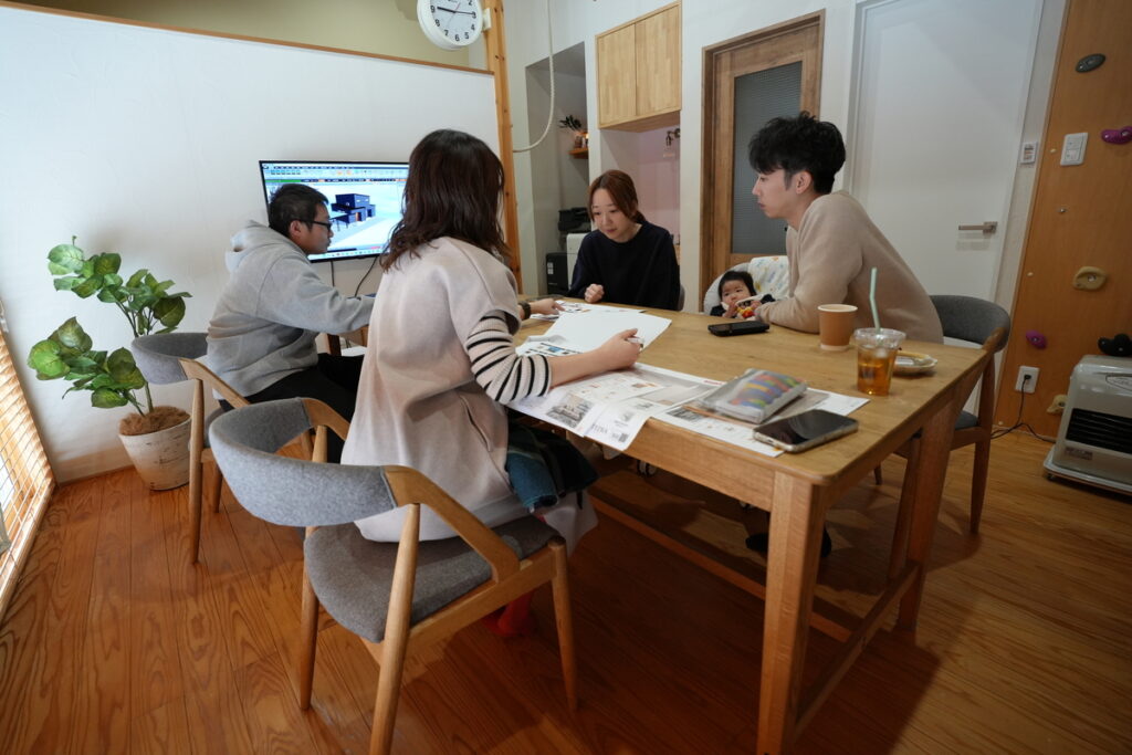 モニターに映る住宅の3Dパースを確認しながら、工務店スタッフと間取りやデザインの打ち合わせを行う赤ちゃんのいるご家族。