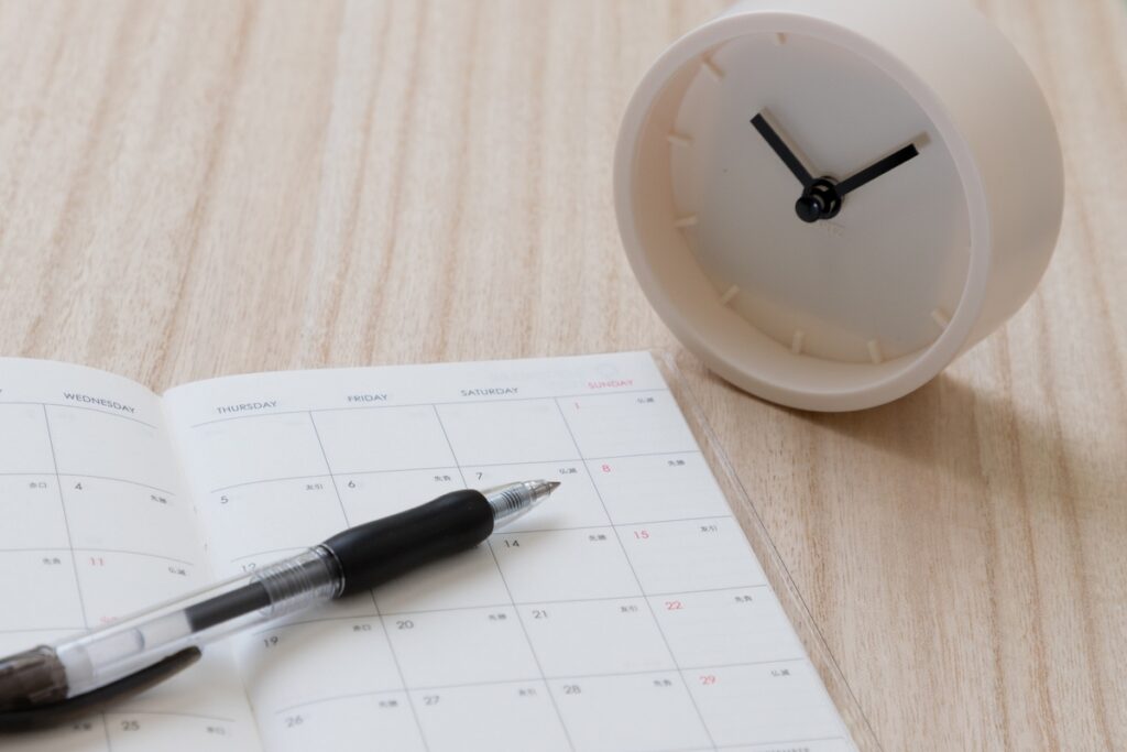 家づくりの工程や打ち合わせの予定が書き込まれたスケジュール帳と、時間を管理するシンプルな置き時計。