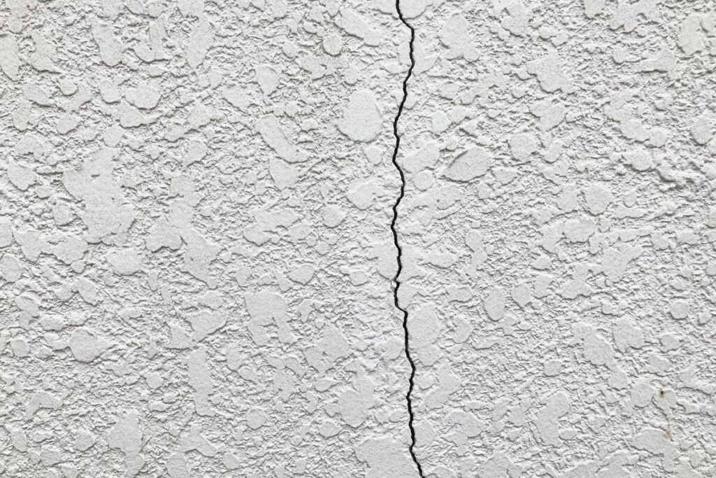 白い塗り壁の外装材に生じた垂直方向の大きなひび割れ（クラック）。補修の必要性を示唆する外壁の劣化状況。