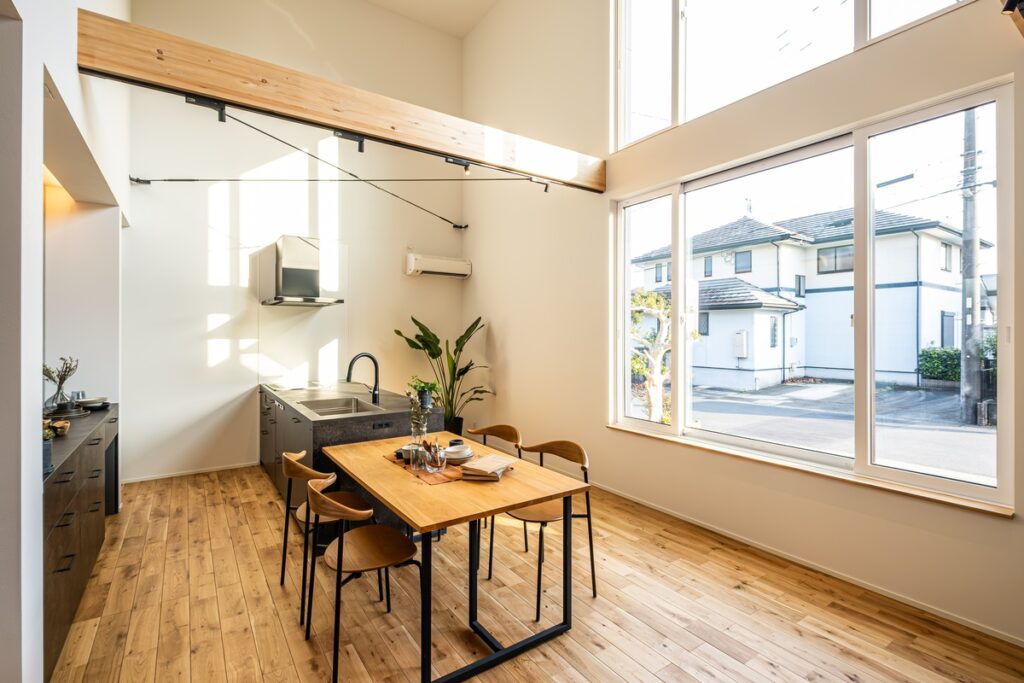 吹抜けの大きな構造梁と大開口サッシが開放感を演出する、陽光溢れるナチュラルモダンなアイランドキッチンとダイニング。