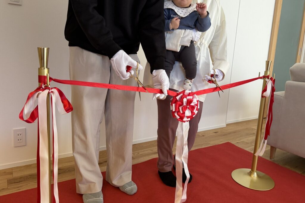待ちに待ったマイホームの完成を祝うテープカットの儀式。赤ちゃんと一緒に、新しい家での豊かな暮らしの門出を祝うご家族。