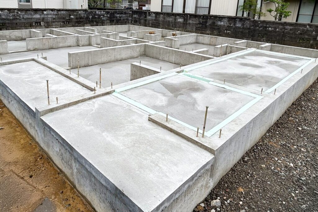アンカーボルトが整然と立ち上がる、打設が完了したばかりの堅牢なベタ基礎。住宅の土台を支える基礎工事の完成状態。