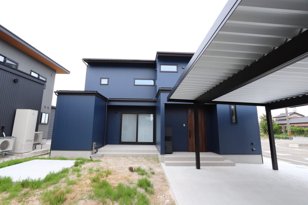 ネイビーのガルバリウム外壁がモダンで都会的な印象を与える外観と、雨や日差しを遮る機能的な大型の折板カーポート。