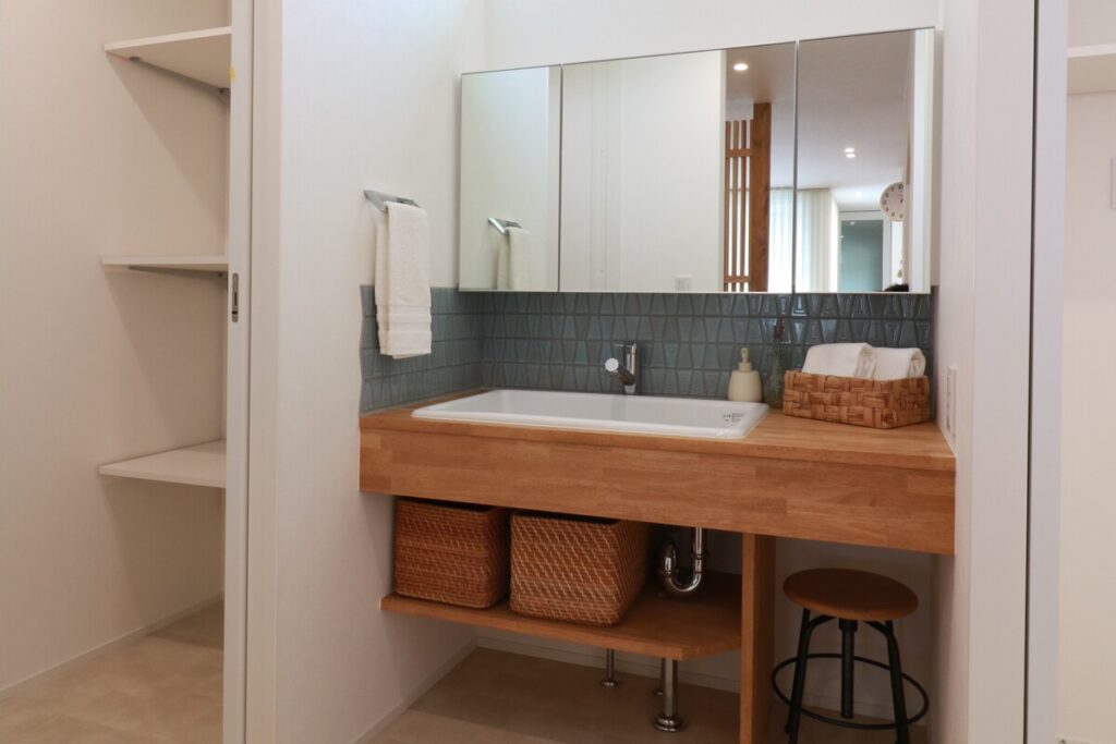 木製カウンターにブルーグレーのタイルを合わせ、下部をバスケット収納にしたナチュラルな造作洗面台。